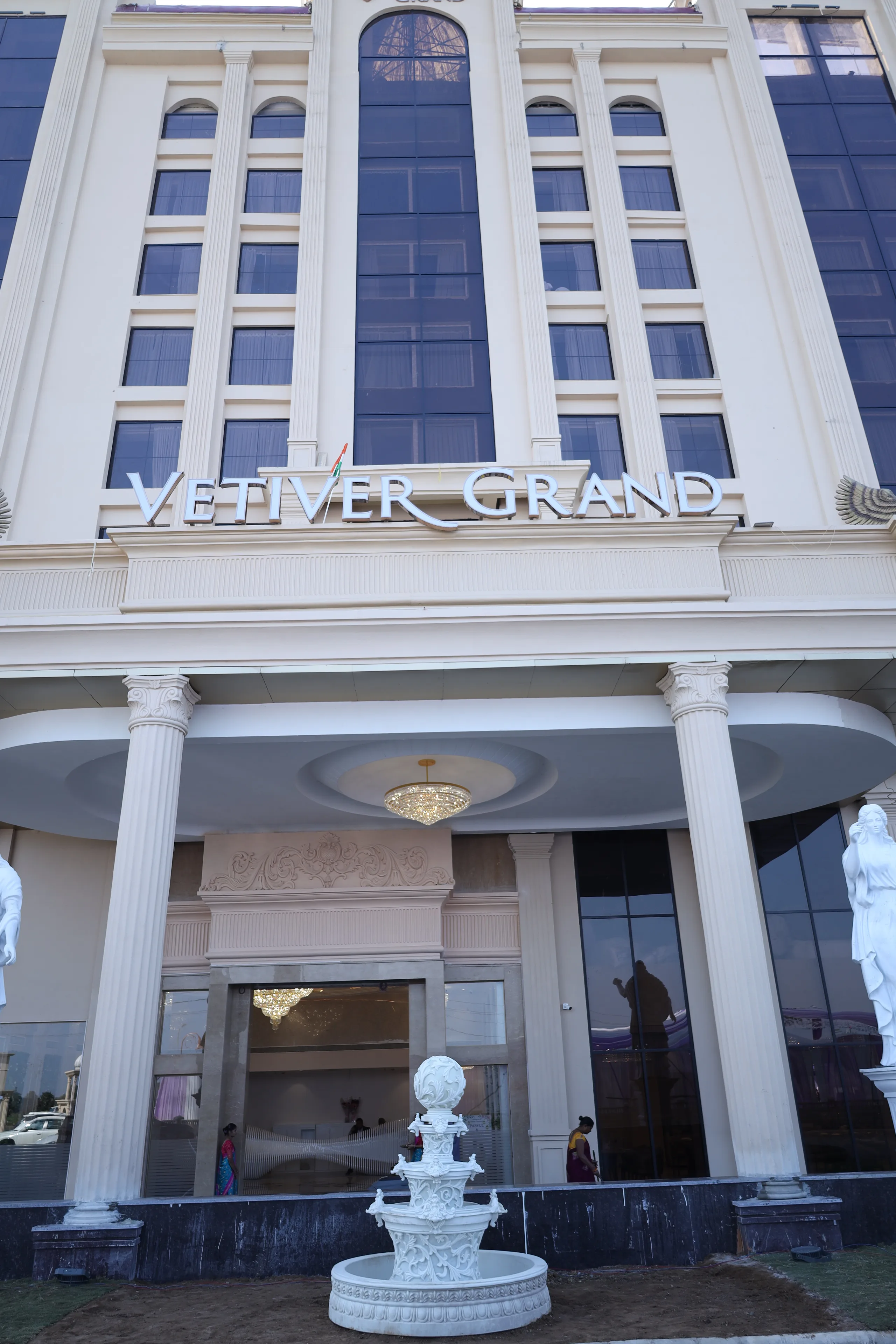 Entrance of Vetiver Grand hotel in Jabalpur: floors of arched windows rising above the Vetiver Grand signage, a chandelier lit under the portico canopy.