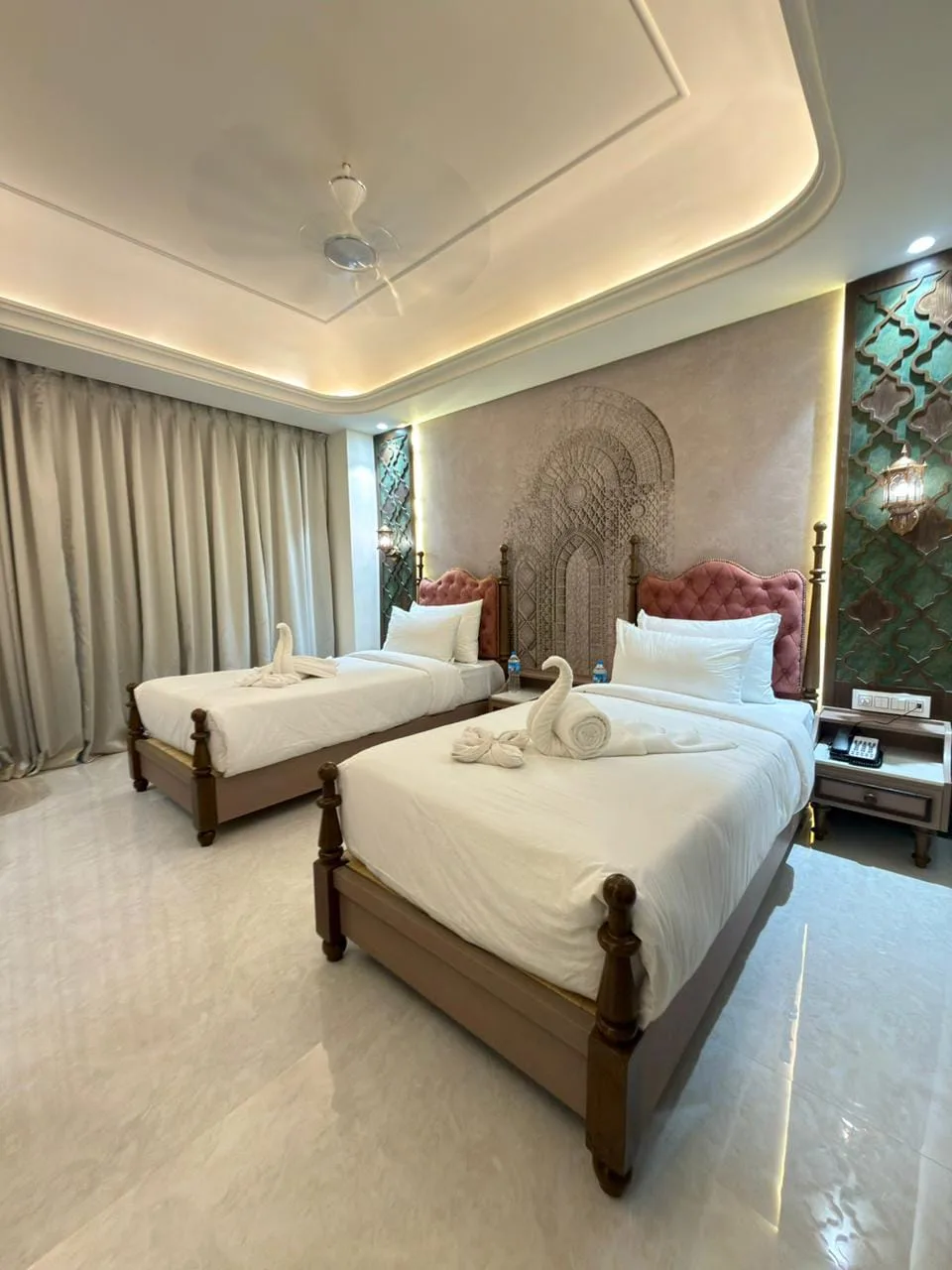 Super Deluxe twin room at Vetiver Grand Jabalpur: pink tufted headboards and teal jaali panels with brass lanterns under warm cove lighting.